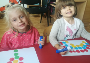Dziewczynki prezentują prace wykonane z kolorowych kropek przyklejonych na kartce papieru